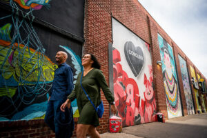 A man and a woman walk on a sidewalk past a colorful mural.