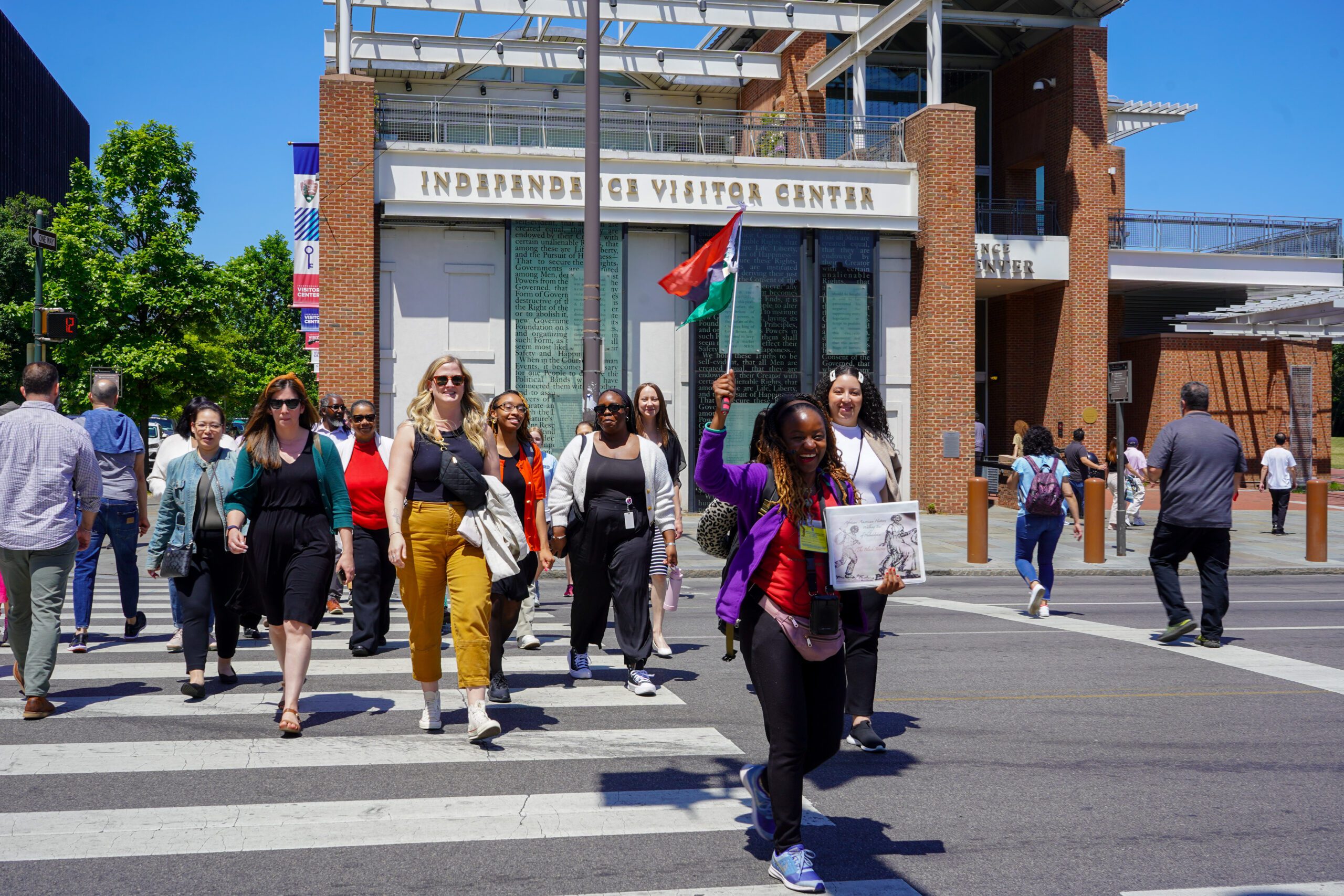 A tour guide from The Black Journey tour leads a group of tourists across the street in from of the Independence Visitor Center.