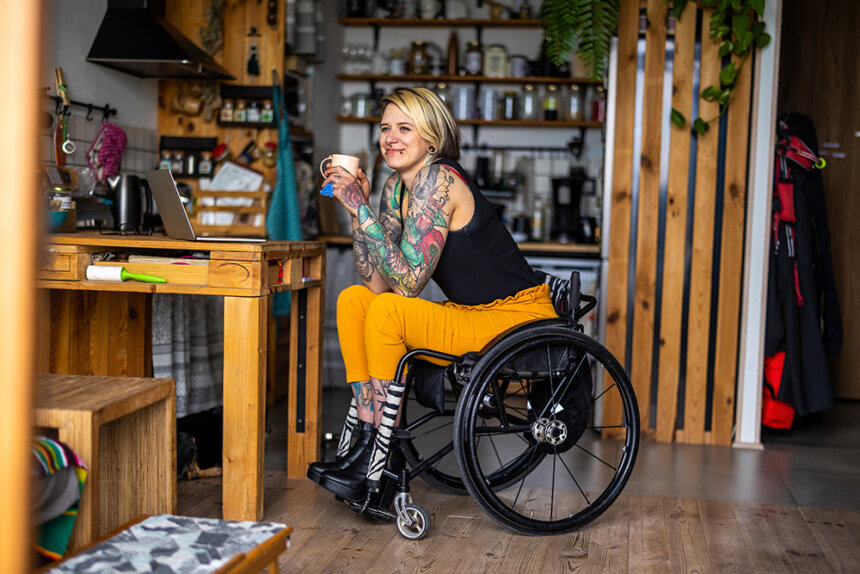 A woman sits in a wheelchair drinking a cup of coffee