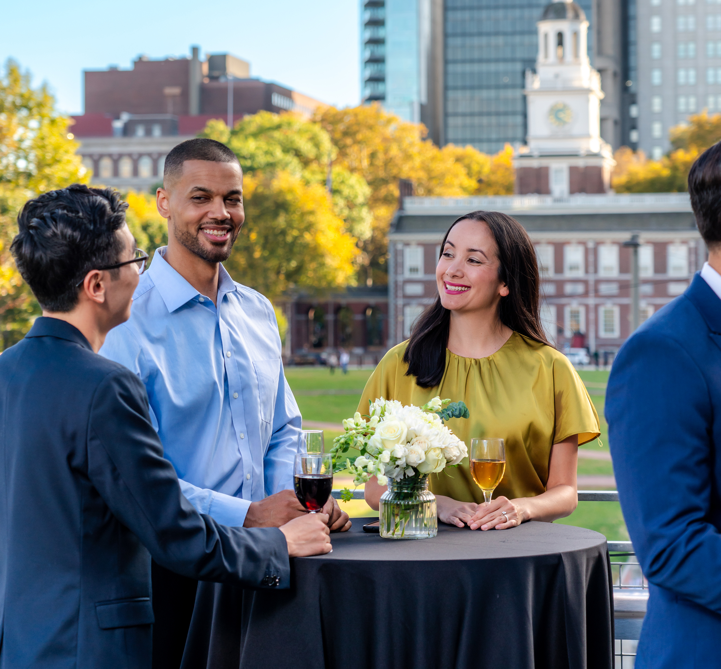 Three people speak with each other around a table. Independence Hall is in the background.