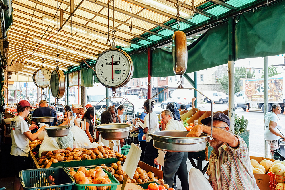 Several shoppers visit the crowded Italian Market and buy various fruits and vegetables from the stands.