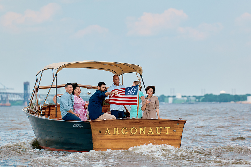 A group of people sit in the back of a wooden boat on the Delaware River.