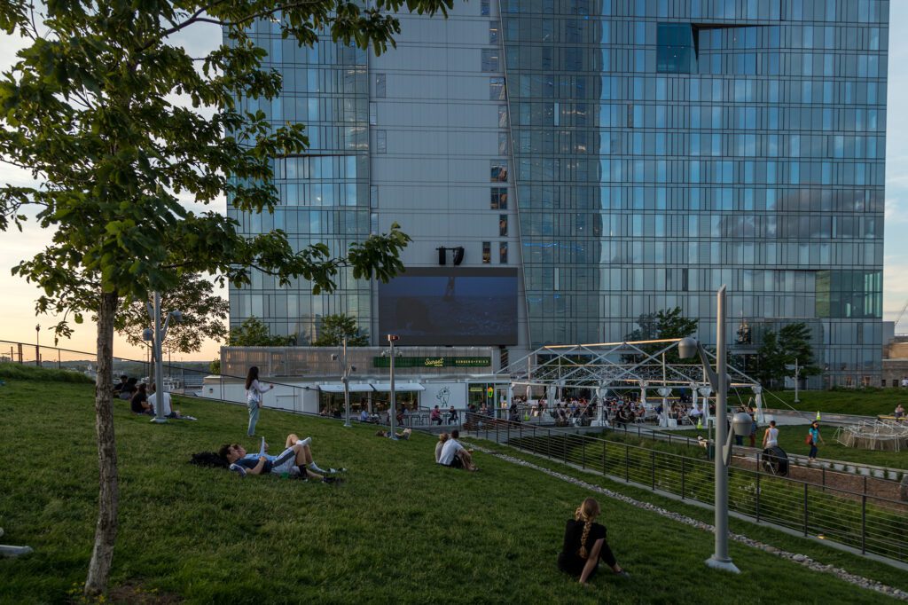 People sitting on the lawn of Cira Green, watching a movie projected onto the building.