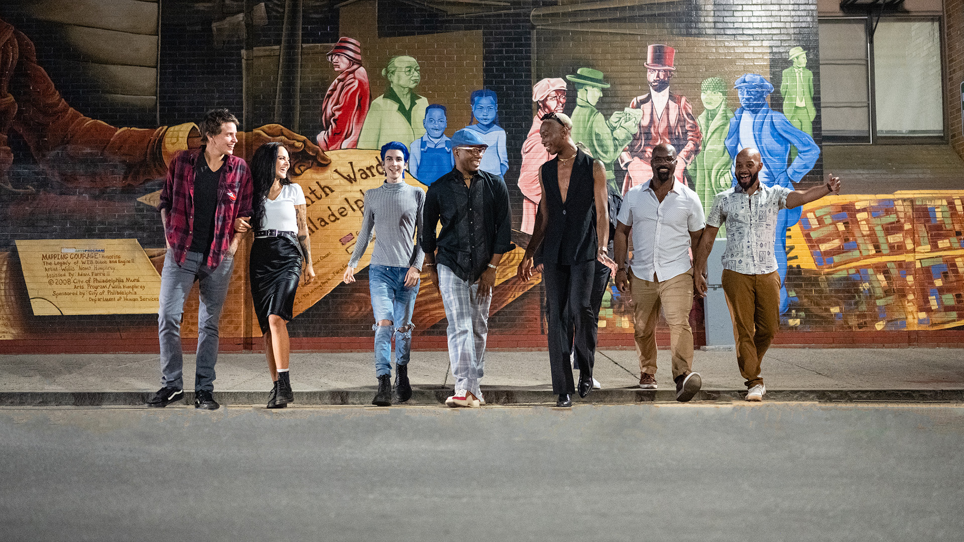 A group of diverse people walk across a street together.