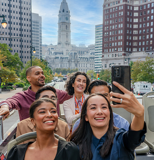 A group of people on a tour bus taking a selfie in front of City Hall.