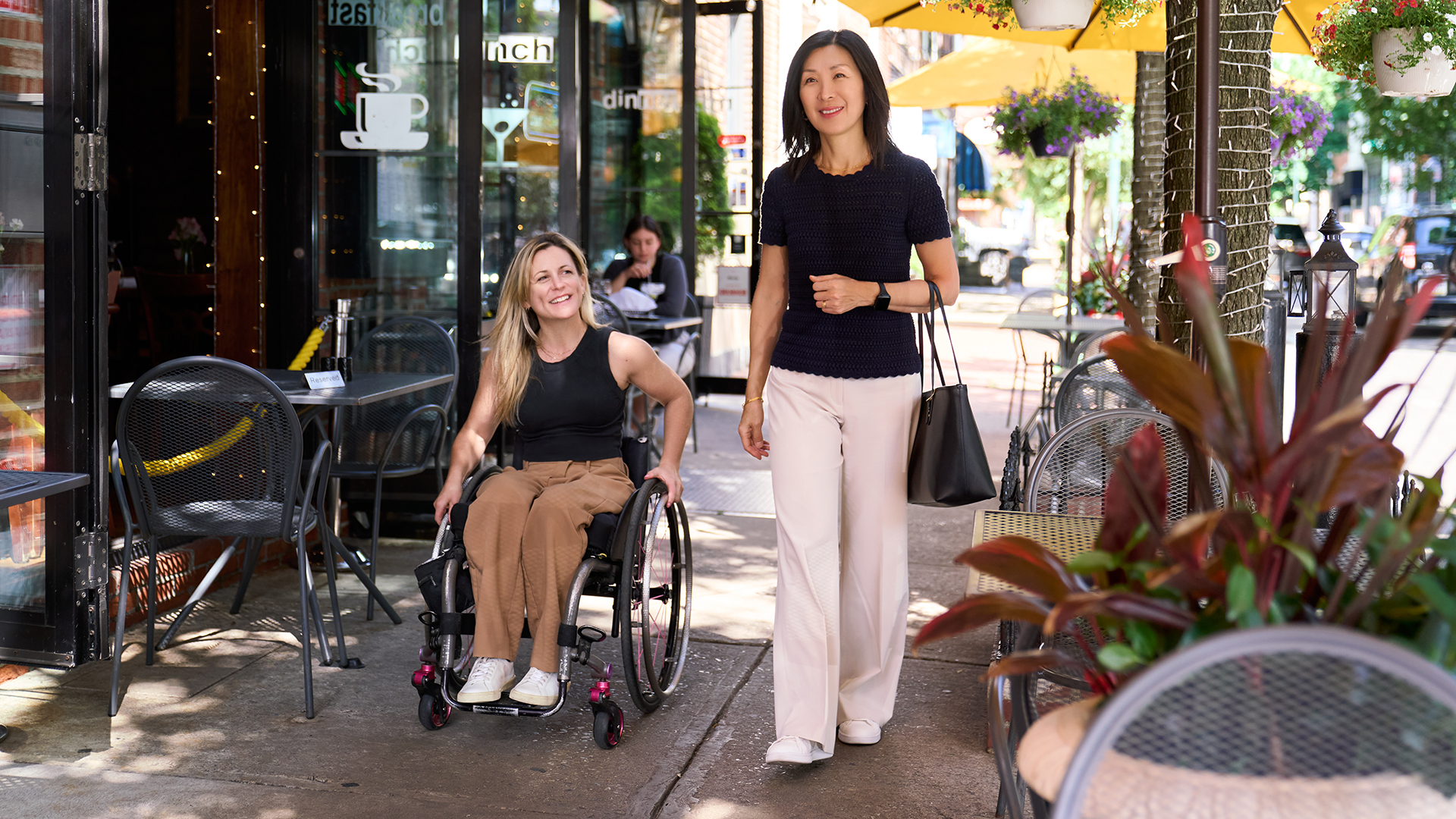 A person in a wheelchair and a person on foot travel down a city sidewalk.