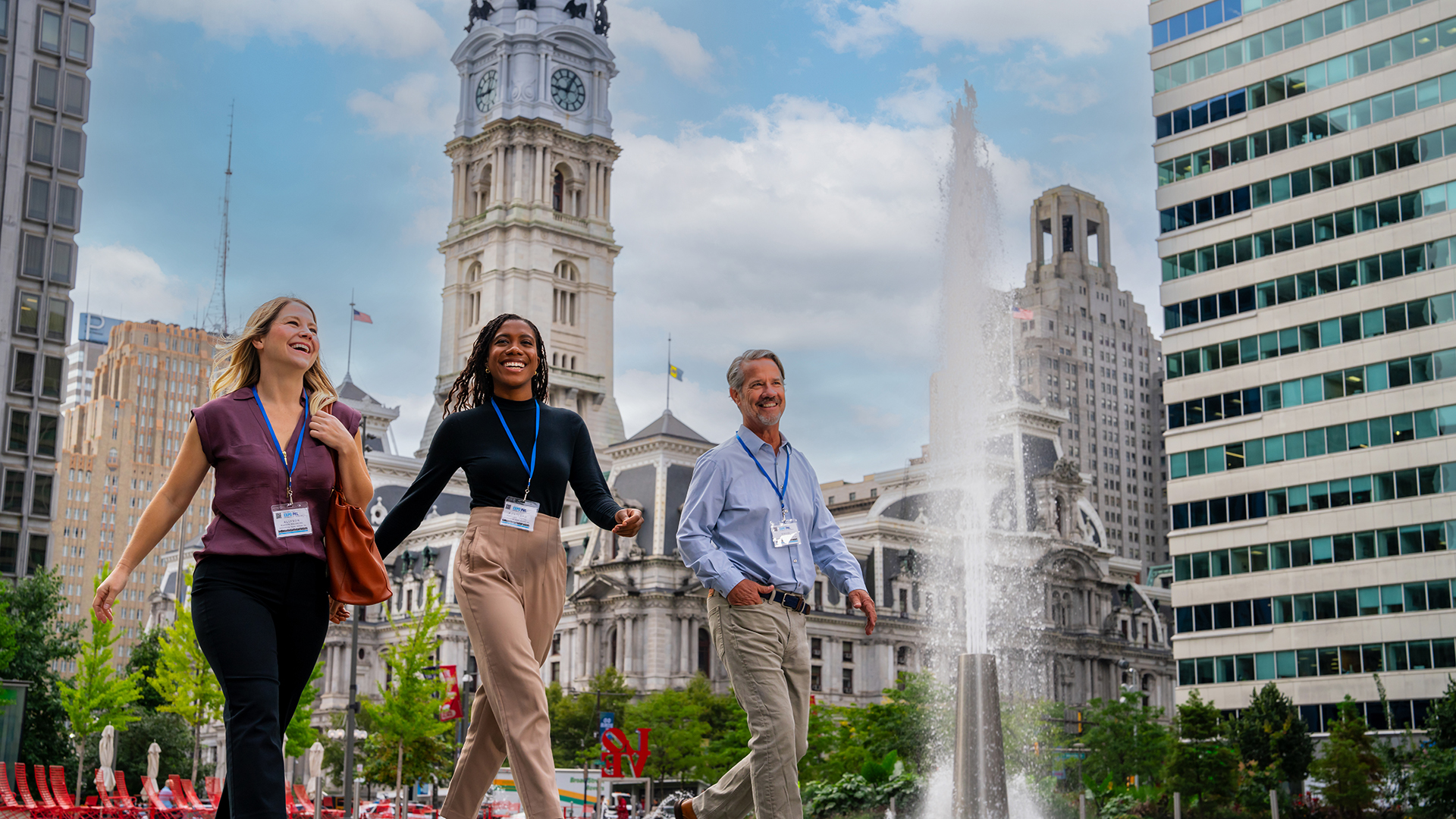 Three people wearing conference badges walk in front of Philadelphia's City Hall.