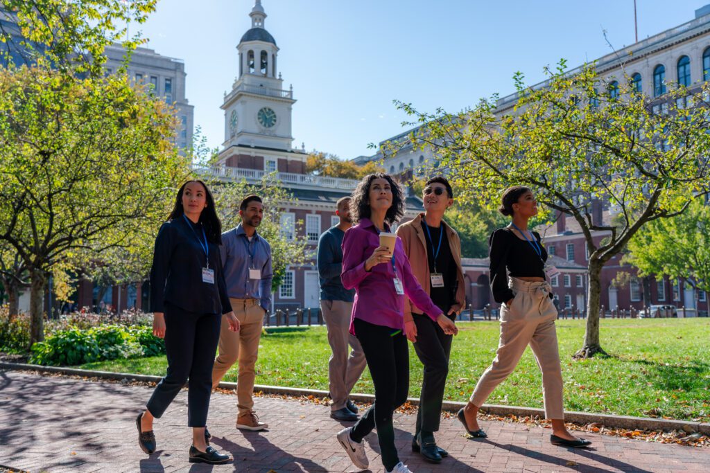 A group of meeting attendees walk past Independence Hall on a sunny day.