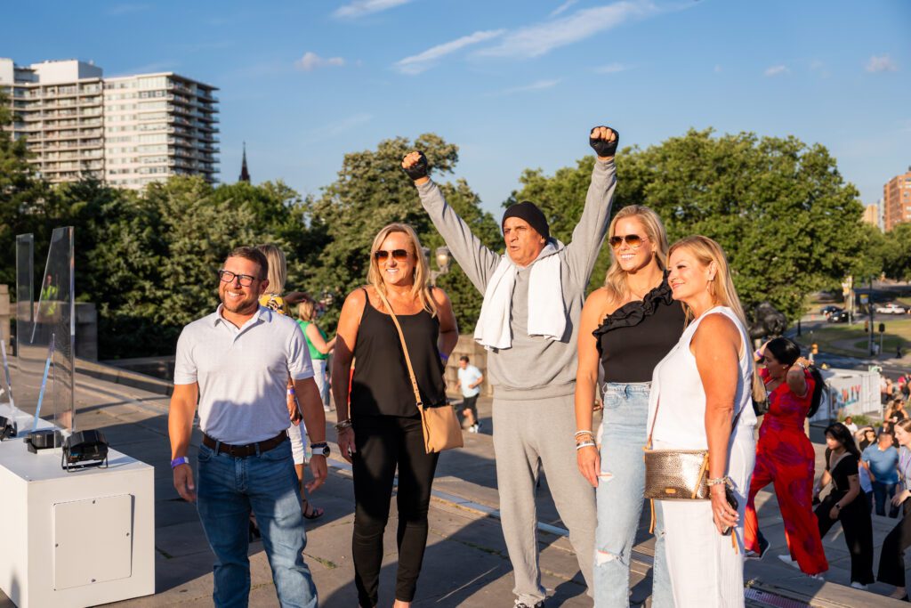 A group of meeting attendees post with a Rocky Balboa impersonator at the NAA Apartmentalize Event at the Philadelphia Museum of Art.