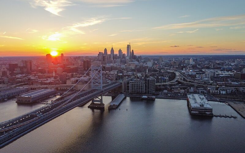 Photo of Philadelphia's skyline in the distance, at sunset, over the Delaware River.