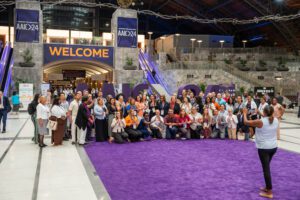 A large group of meeting attendees pose in from of the AAIC 2024 sign inside the Grand Hall of the Pennsylvania Convention Center.