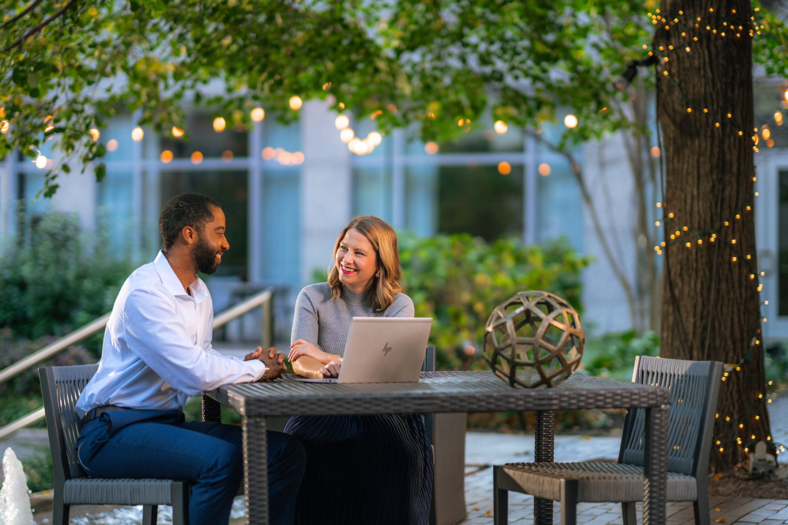 Two people meeting outside, sitting at at table with a laptop