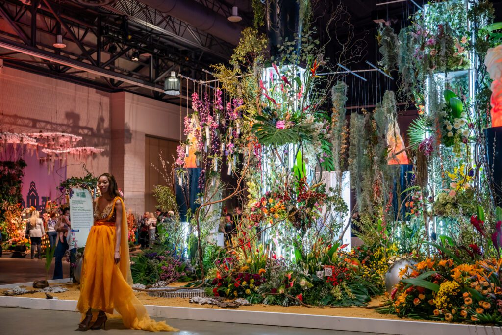 A person posing next to an expansive flower display,.